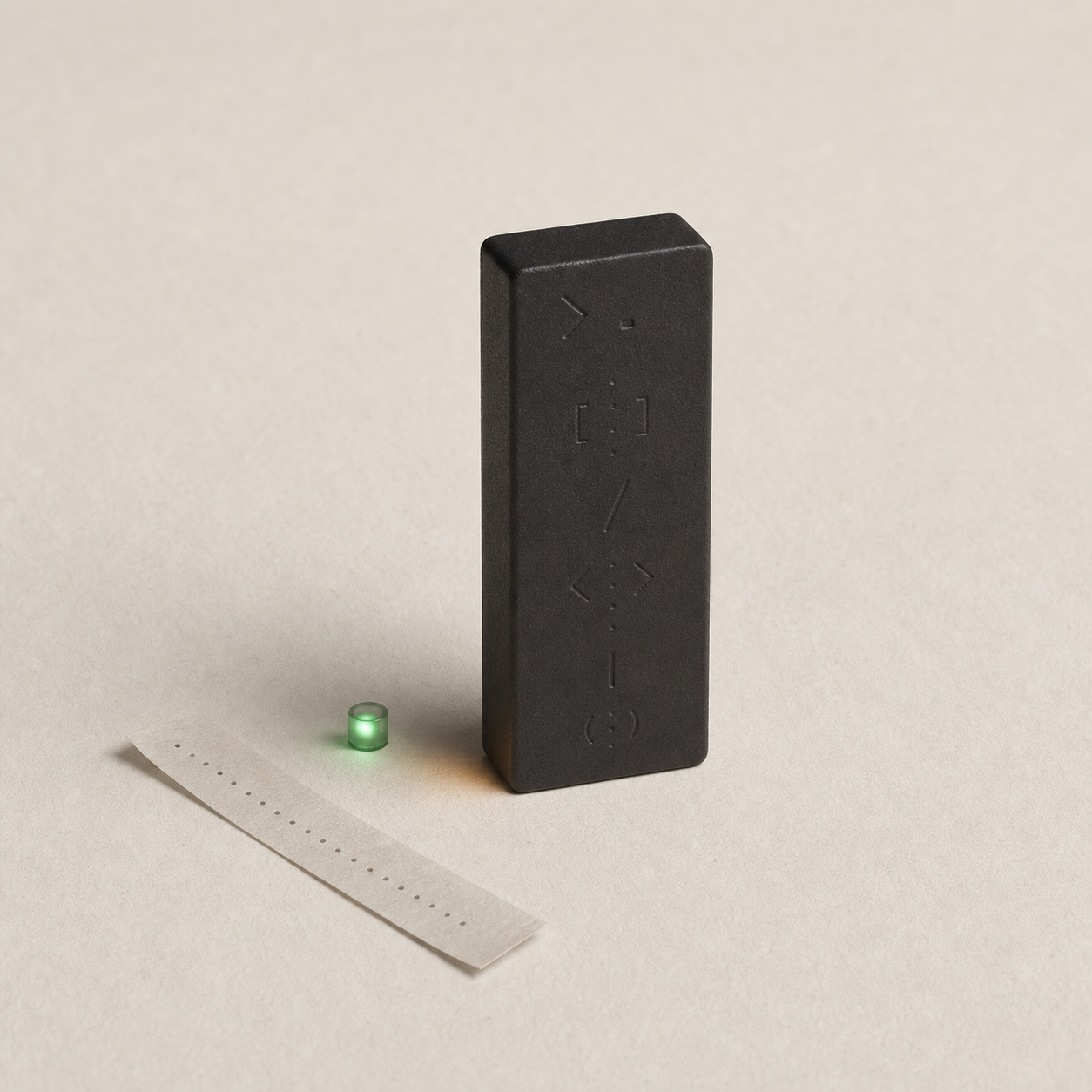 A small matte black terminal cursor block with faint embossed command marks, a green verification light, and a thin paper strip.